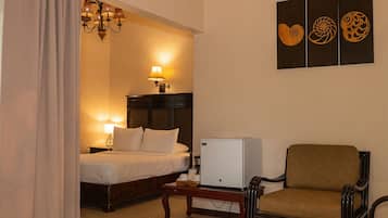 Une chambre d’hôtel avec un lit, une petite table, une chaise, un réfrigérateur et des œuvres d’art murales.