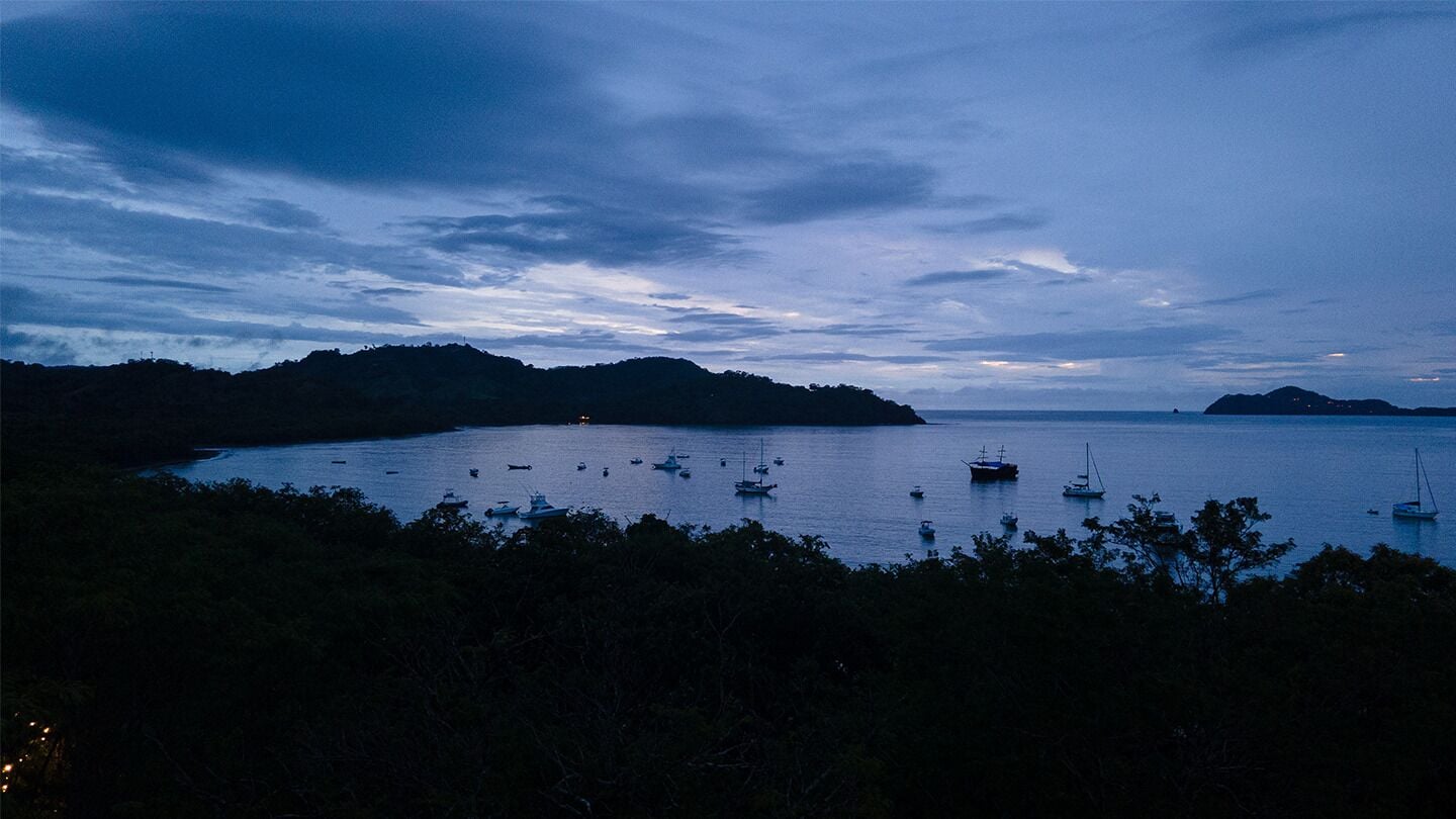 A coastal scene with boats on calm water, surrounded by hills and dense vegetation.