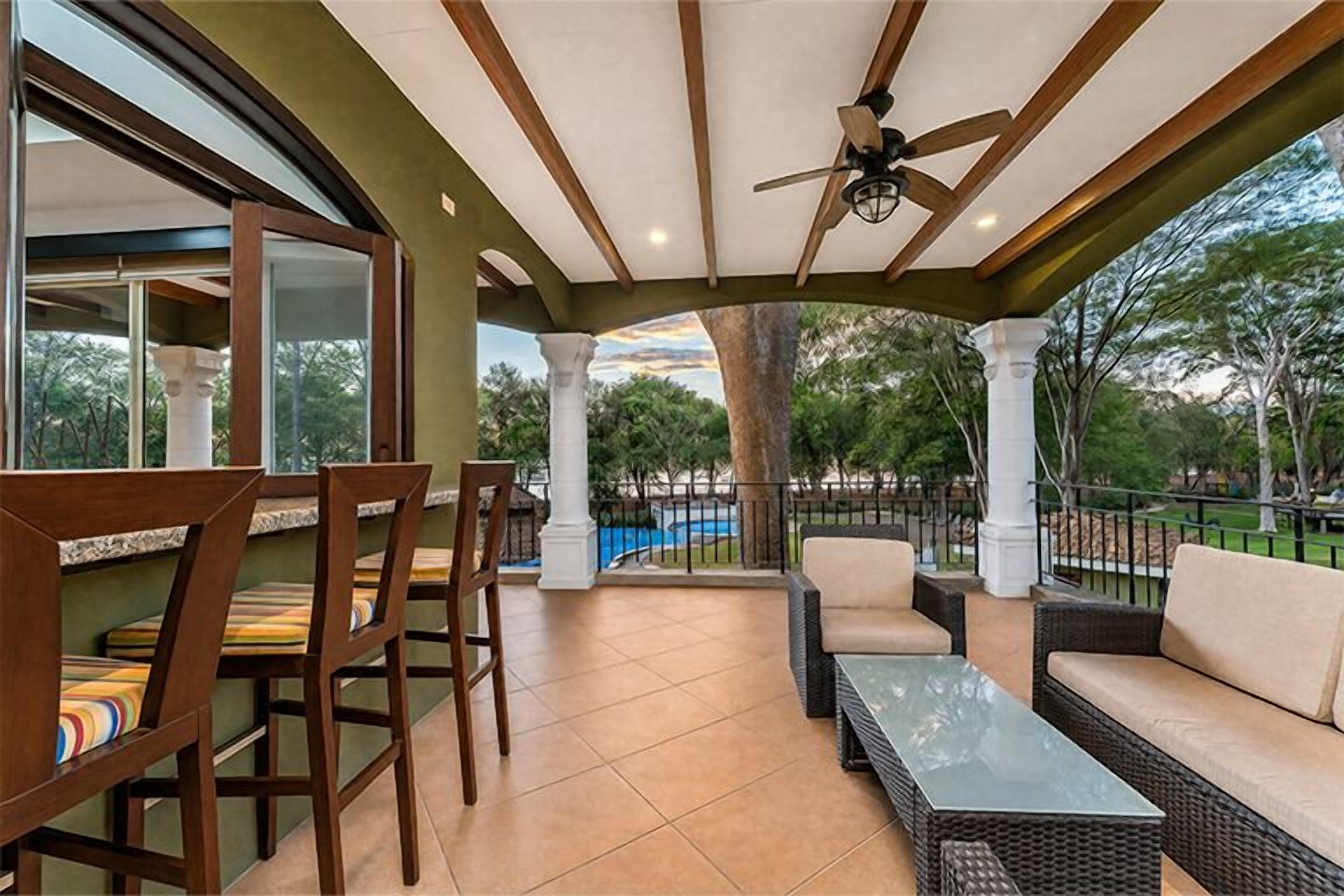 An outdoor patio with wicker furniture, a glass-top table, and a ceiling fan.