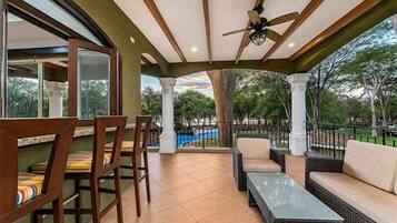An outdoor patio with wicker furniture, a glass-top table, and a ceiling fan.