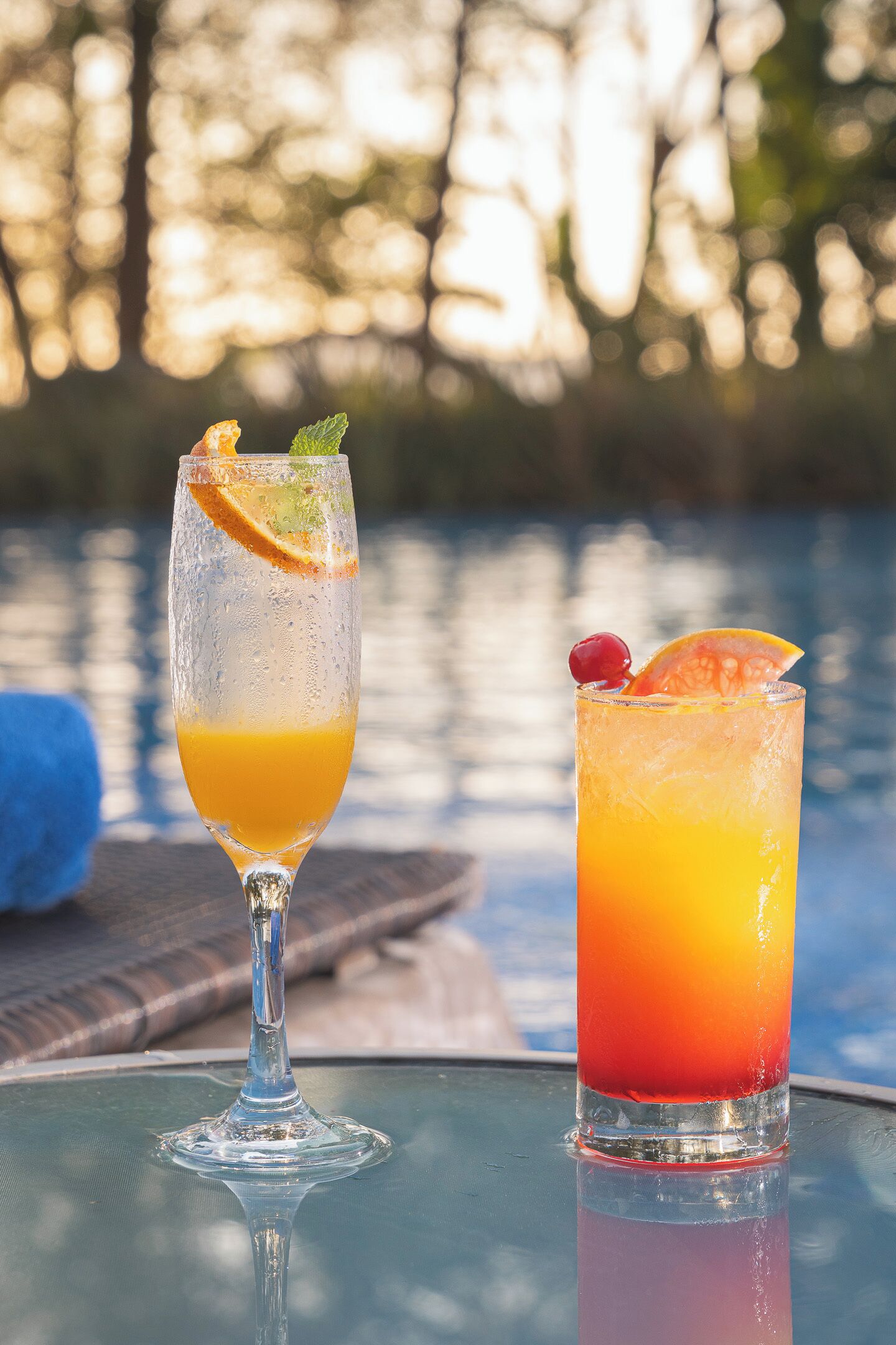 Two glasses of beverages on a table near a pool.