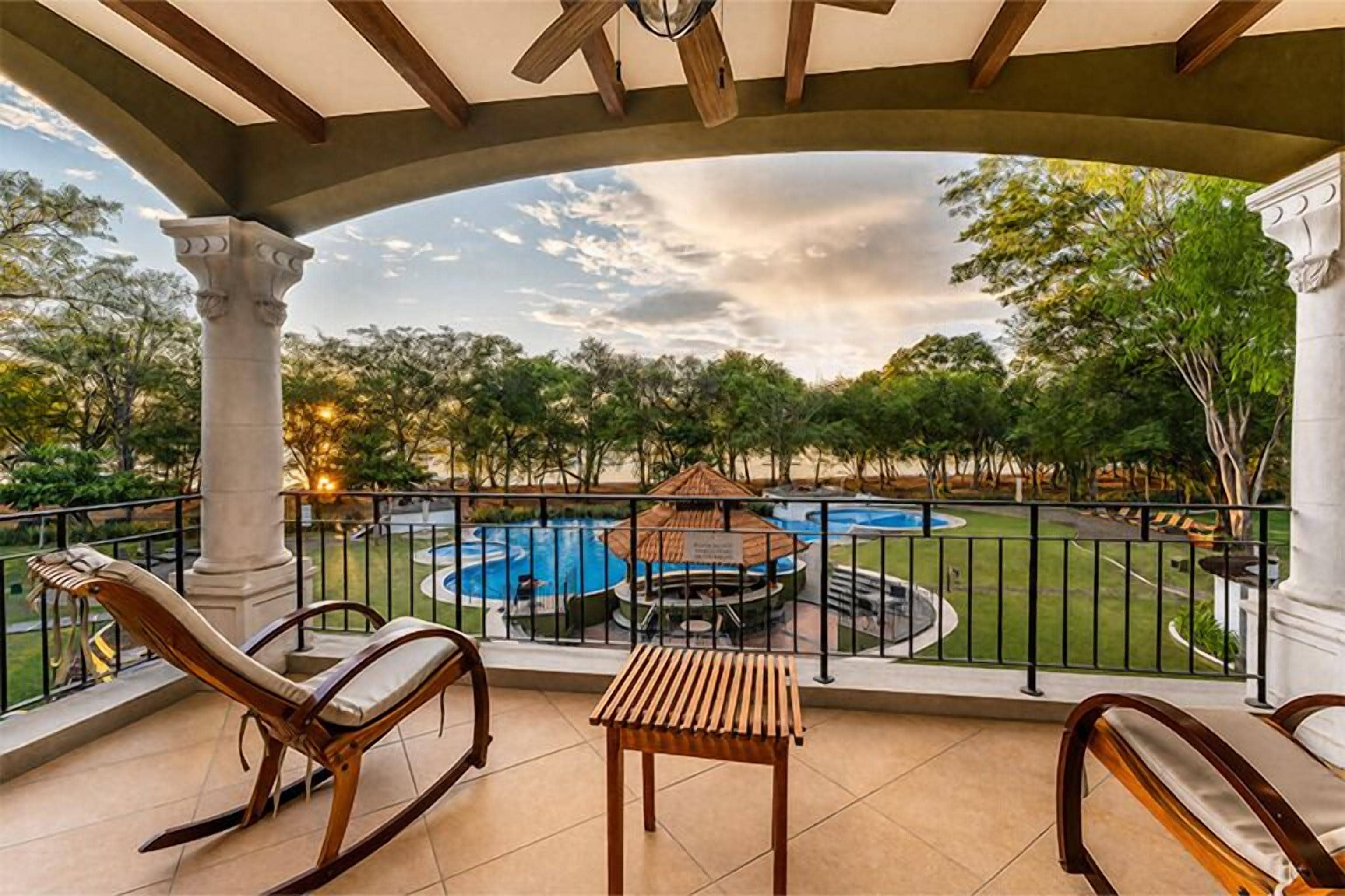 Un balcon avec deux fauteuils à bascule, une petite table et une vue sur une piscine et un jardin.