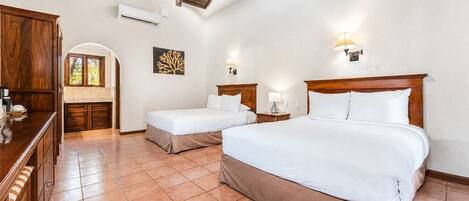 A hotel room with two beds, a wooden wardrobe, a tiled floor, and a ceiling with exposed beams.