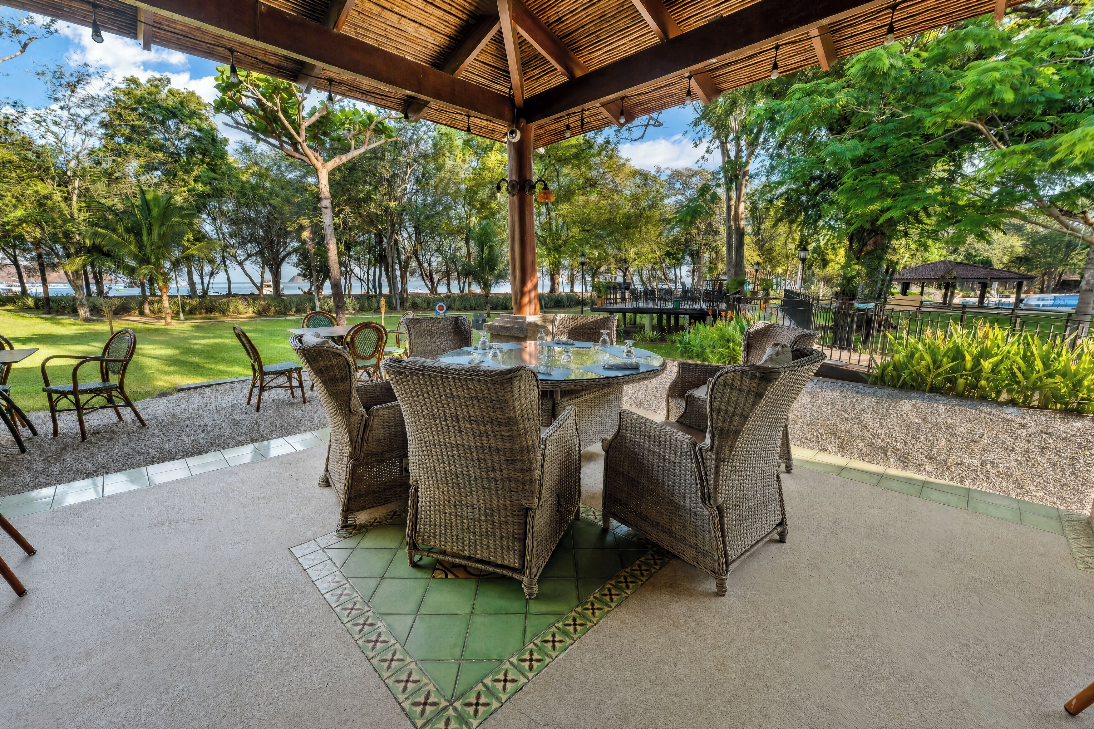 An outdoor patio with wicker furniture, a glass-top table, and a view of the sea.