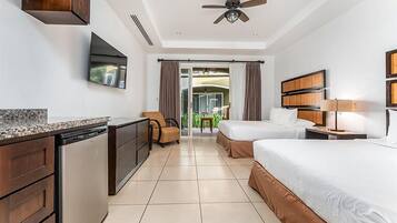 A hotel room with a kitchenette, two beds, a TV, and a ceiling fan.