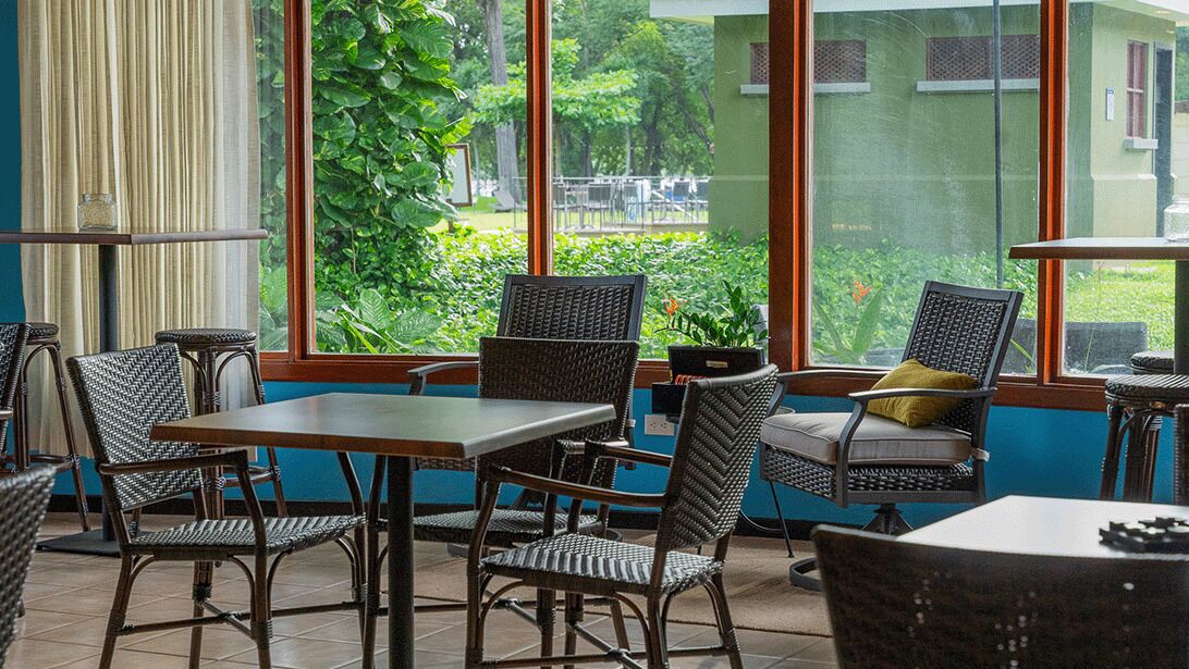 An indoor seating area with wicker furniture, a table, and a view of greenery outside.