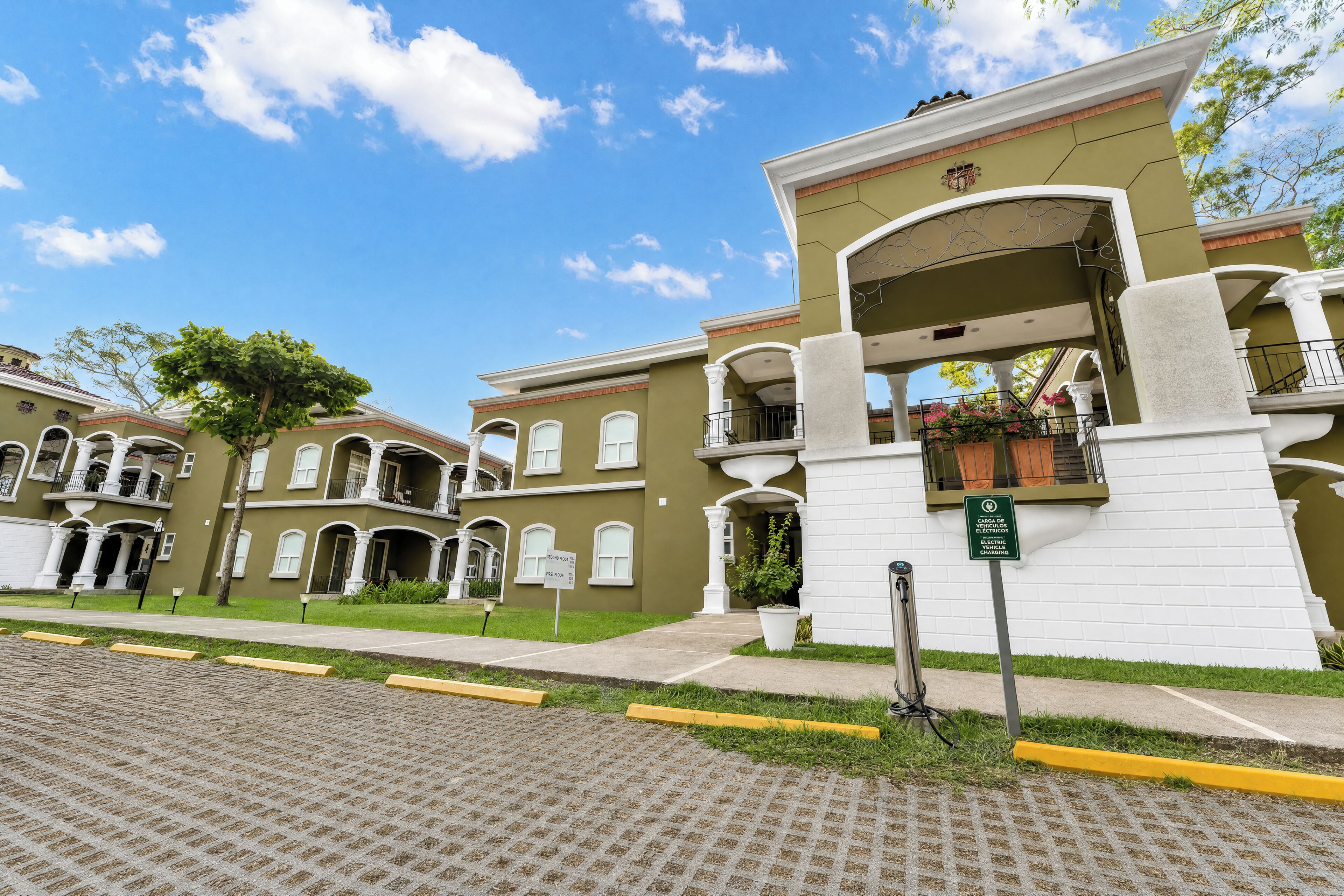 A multi-story building with a green facade, white columns, and balconies with potted plants.