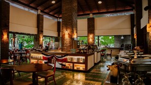 A restaurant with a central bar area, multiple seating options, and large windows providing views of greenery.