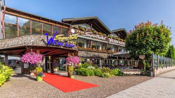 A hotel with a red carpet entrance, flower arrangements, and a sign reading "Wilder Kaiser Sporthotel."