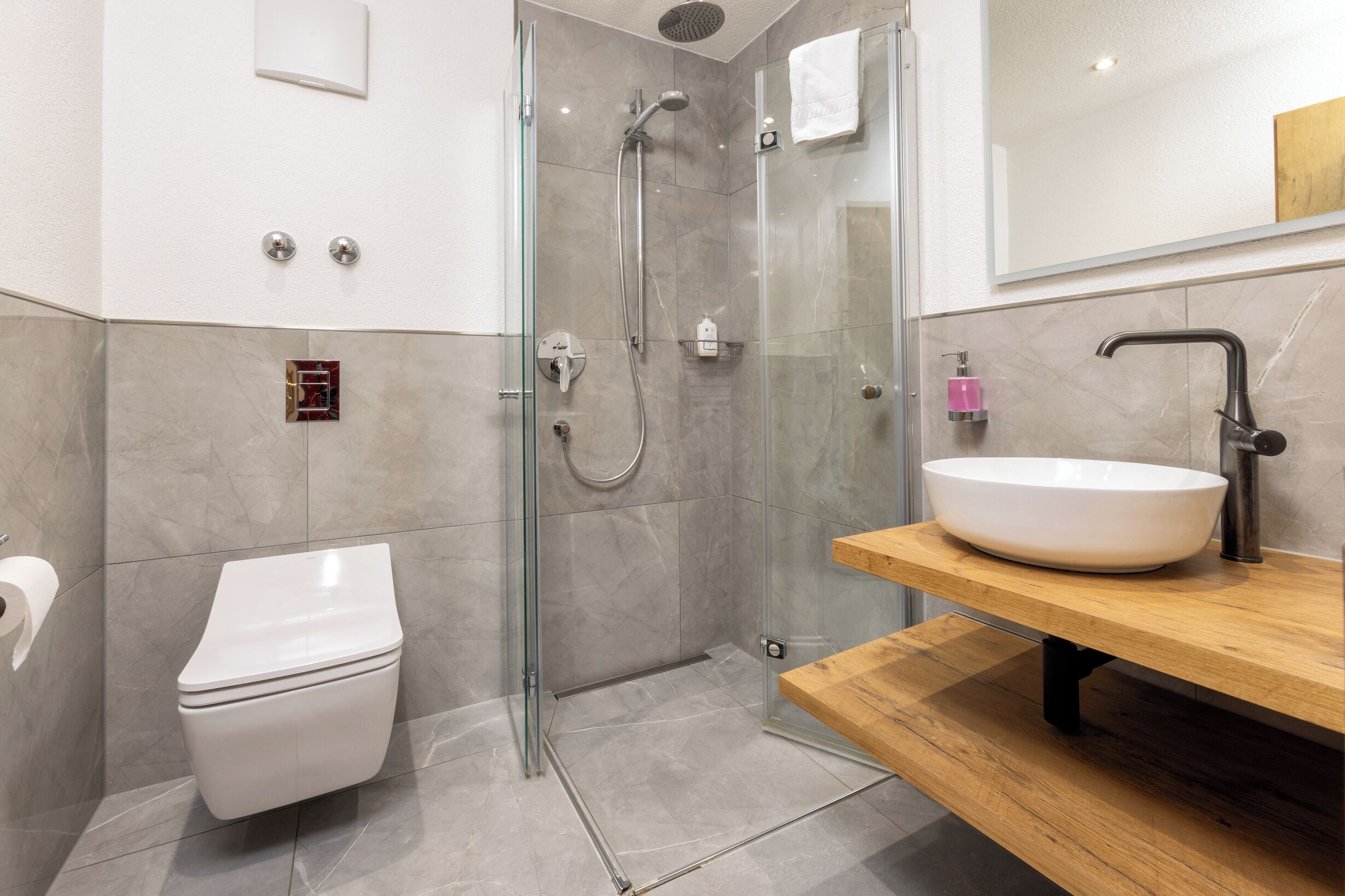 Ein modernes Badezimmer mit einer Glaskabine zur Dusche, einer weißen Toilette und einem Holzausleger mit einem großen Waschbecken.