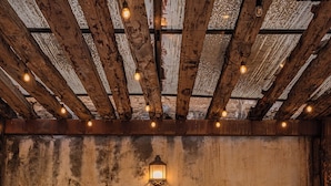 A rustic interior with exposed wooden beams, a central table with a vase of flowers, wicker furniture, and a wall-mounted light fixture. - Hotel De La Parra (Oaxaca)