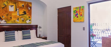 A bedroom with a bed, a nightstand, a wooden wardrobe, and two colorful paintings on the walls.