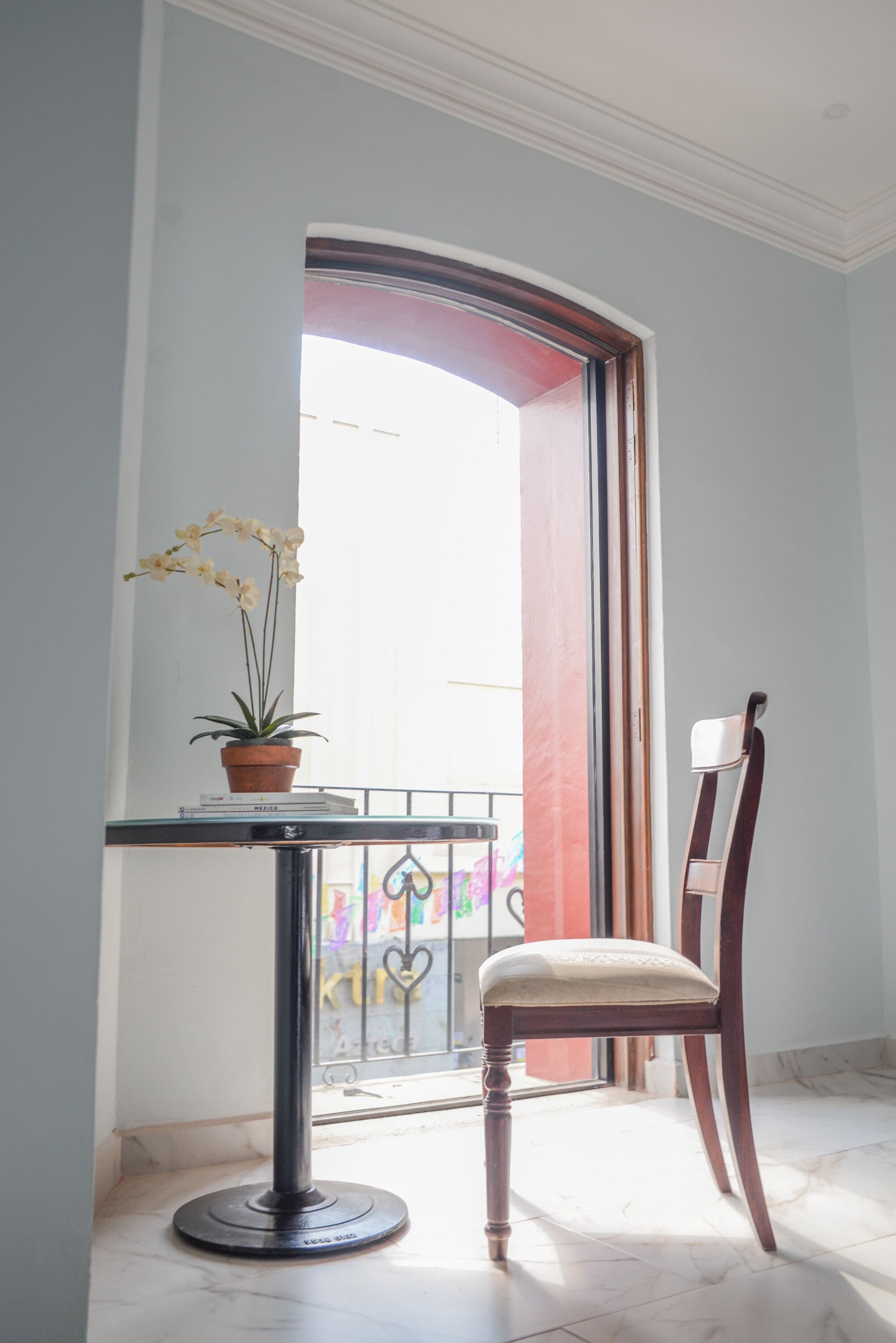 A balcony with a potted orchid, a chair, and a view of a colorful building through a glass door.
