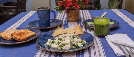 A table set with food and drinks, including toast, cheese, and a green smoothie, with a blue tablecloth and a vase of red flowers.