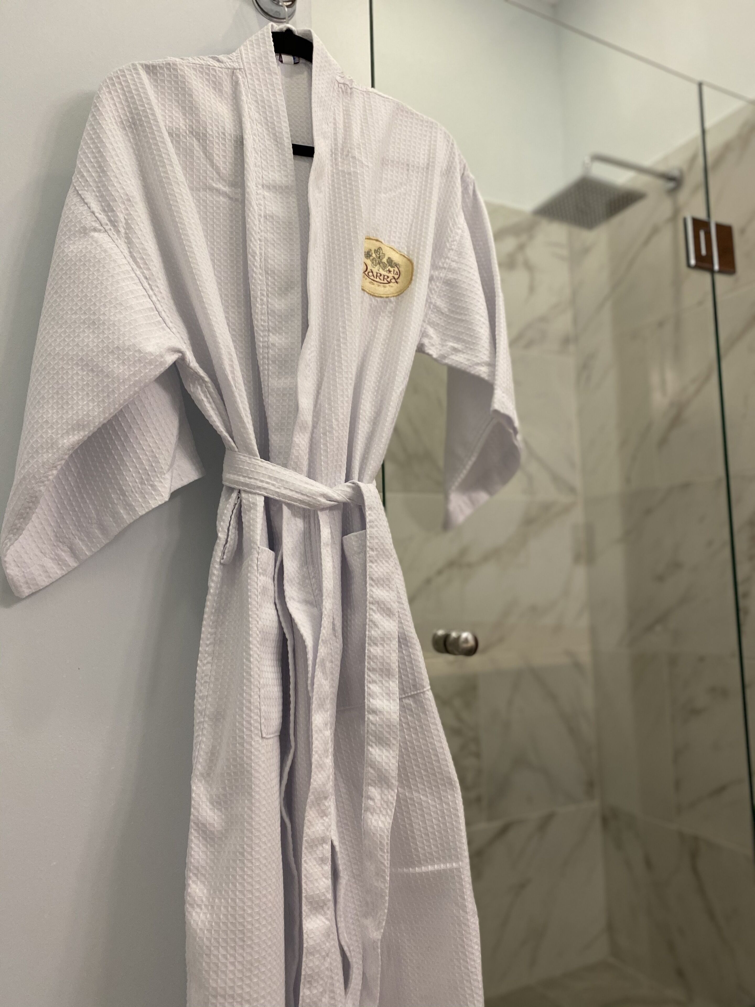 A white robe hanging on a wall in a bathroom with a glass shower door.