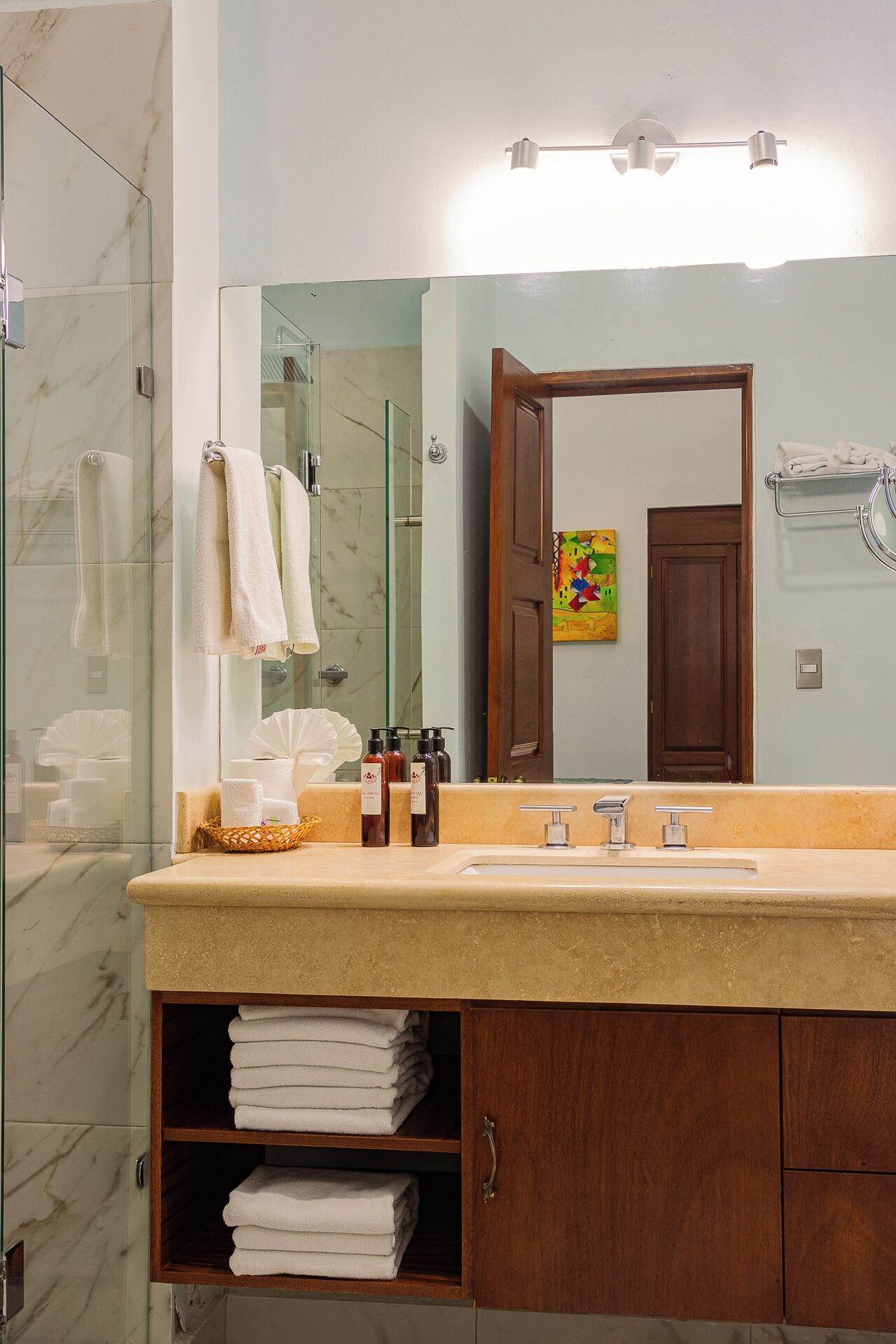 Une salle de bain avec une douche en marbre, un lavabo avec un miroir et un meuble en bois contenant des serviettes.