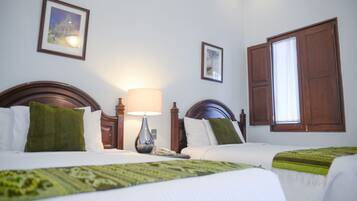 A hotel room with two beds, a nightstand with a lamp, and a window with wooden shutters.