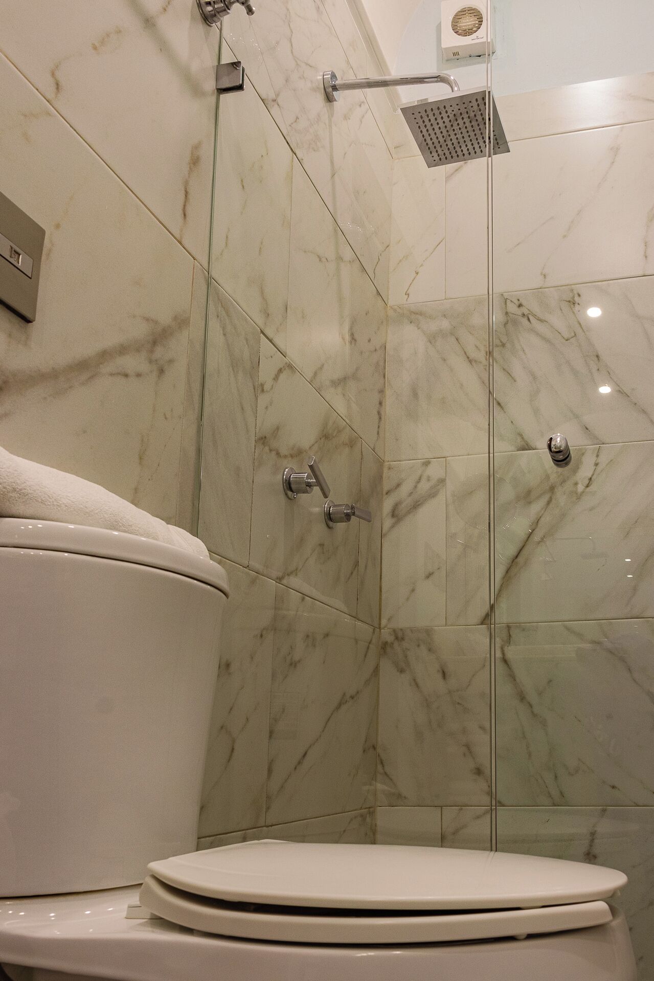 A bathroom with a toilet, a shower enclosure, and a marble-tiled wall.