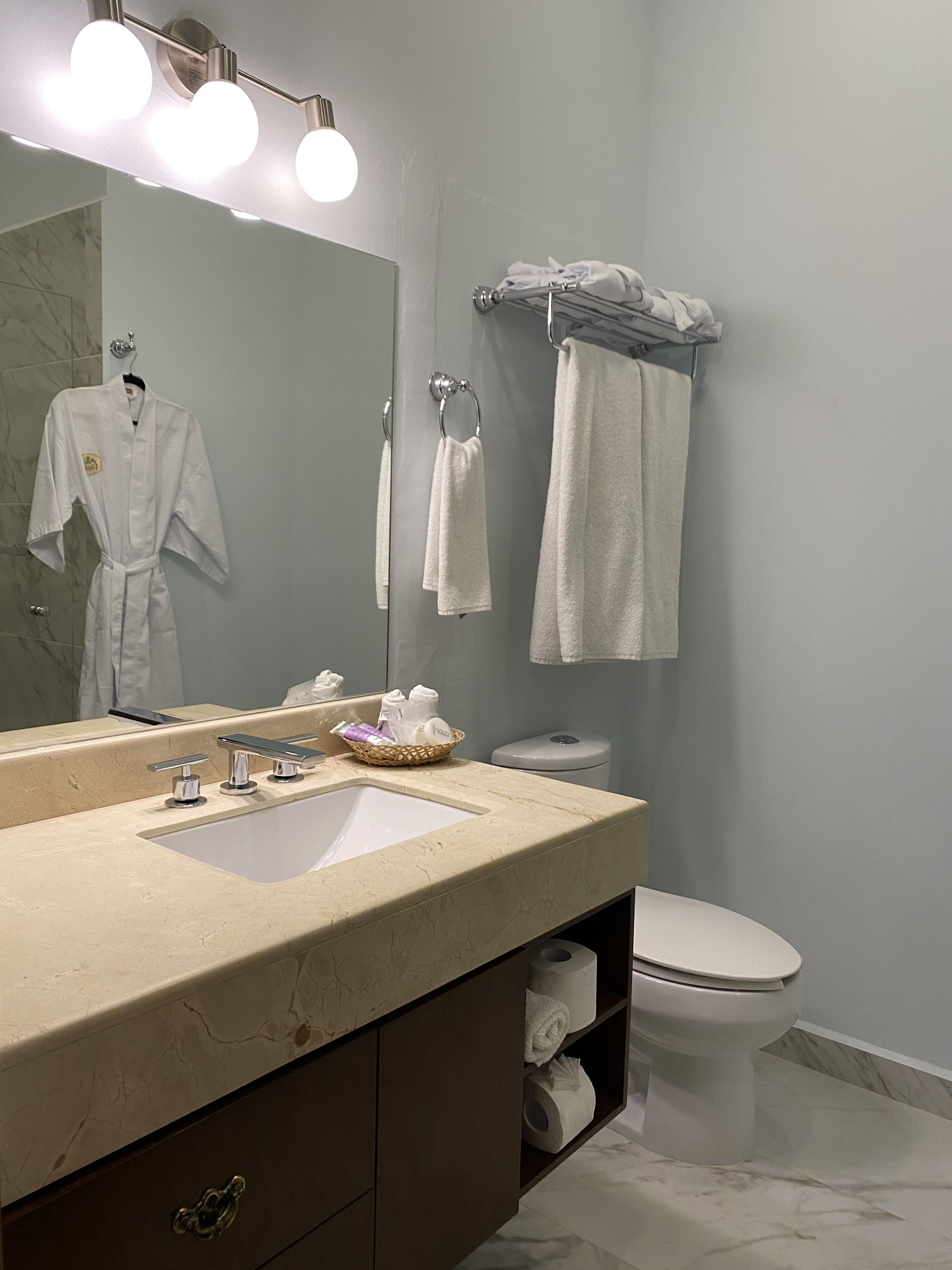 Un baño moderno con lavamanos de mármol, un espejo grande y un inodoro.