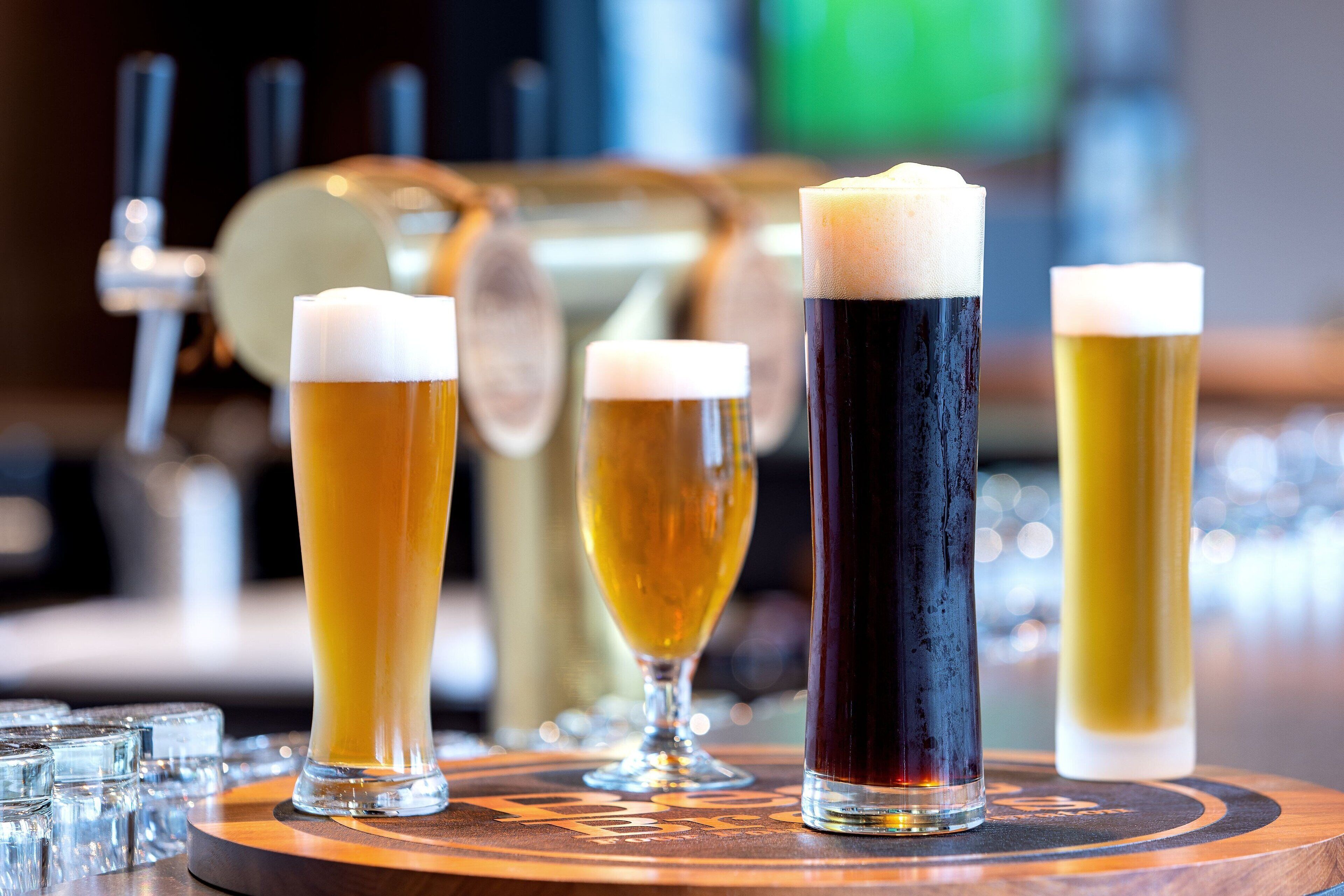 Four glasses of beer on a coaster with a bar in the background.