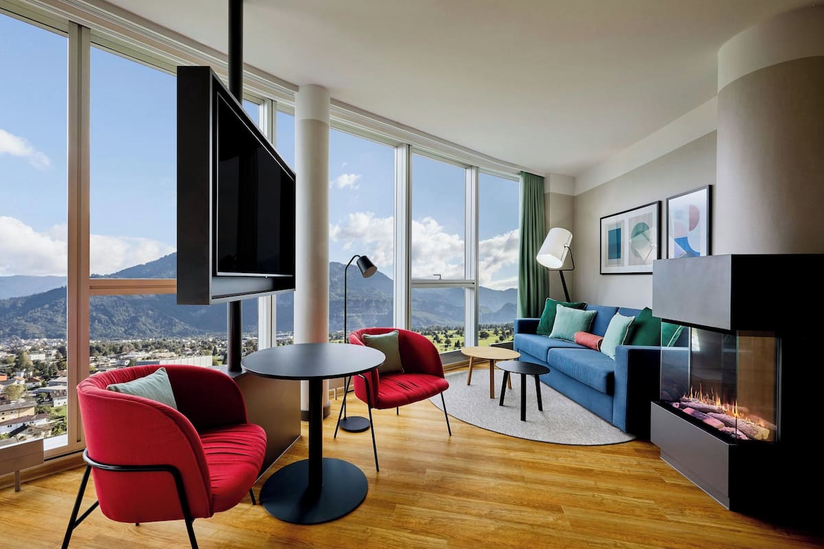 Un salon moderne doté d’une grande fenêtre, d’un téléviseur à écran plat, d’une cheminée et d’un canapé agrémenté de coussins colorés.