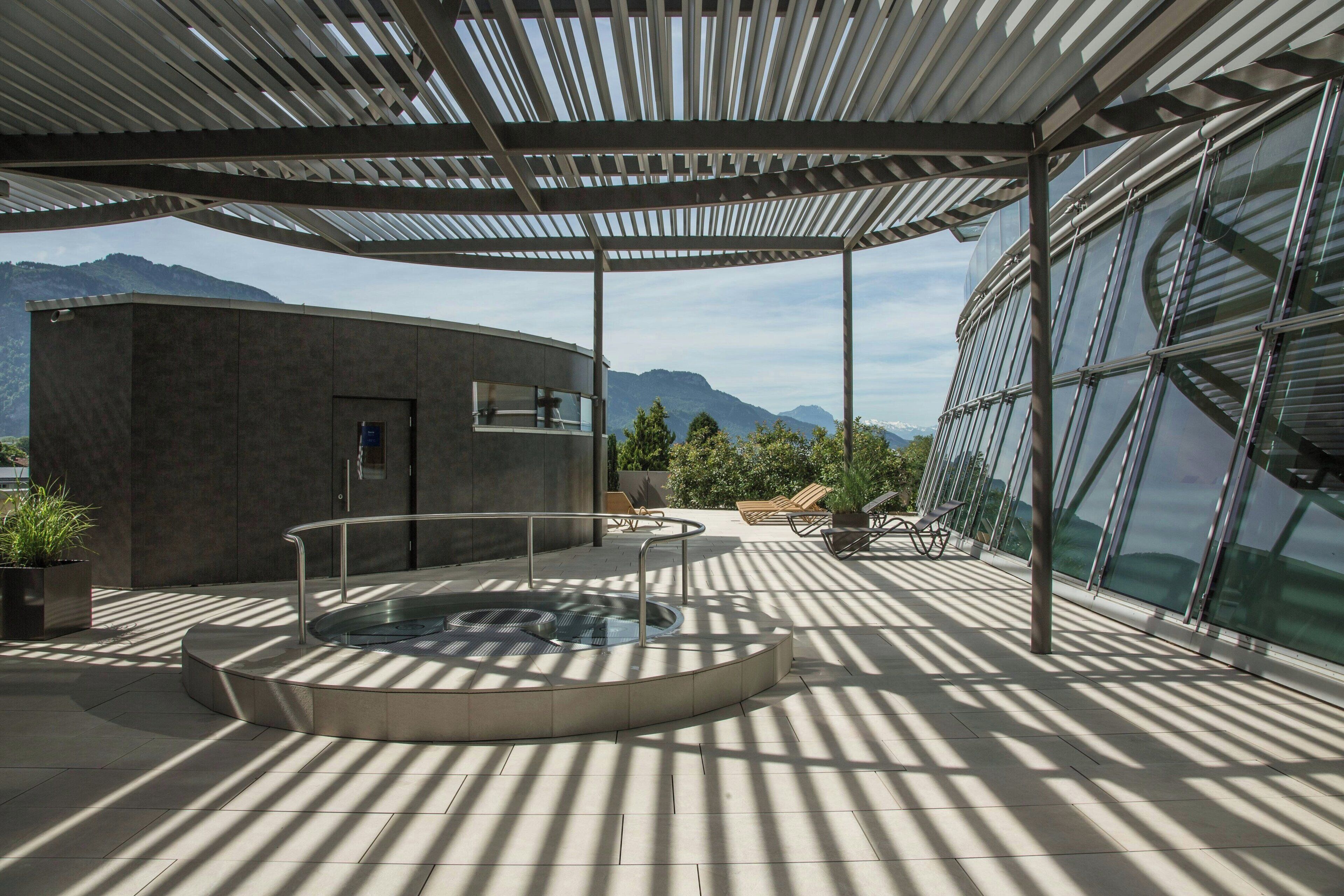 A modern outdoor area with a circular hot tub, seating, and a view of mountains.