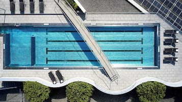 Vista aérea de una piscina con tobogán, tumbonas y paneles solares.