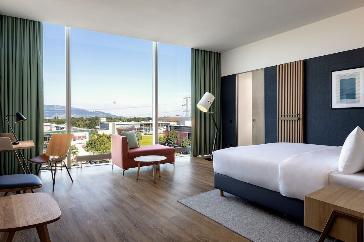 Une chambre d’hôtel moderne, dotée d’un grand lit, d’un bureau, d’une chaise et offrant une vue sur la ville.