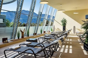 Un espacio interior con asientos iluminado por el sol y vistas a las montañas a través de grandes ventanales.