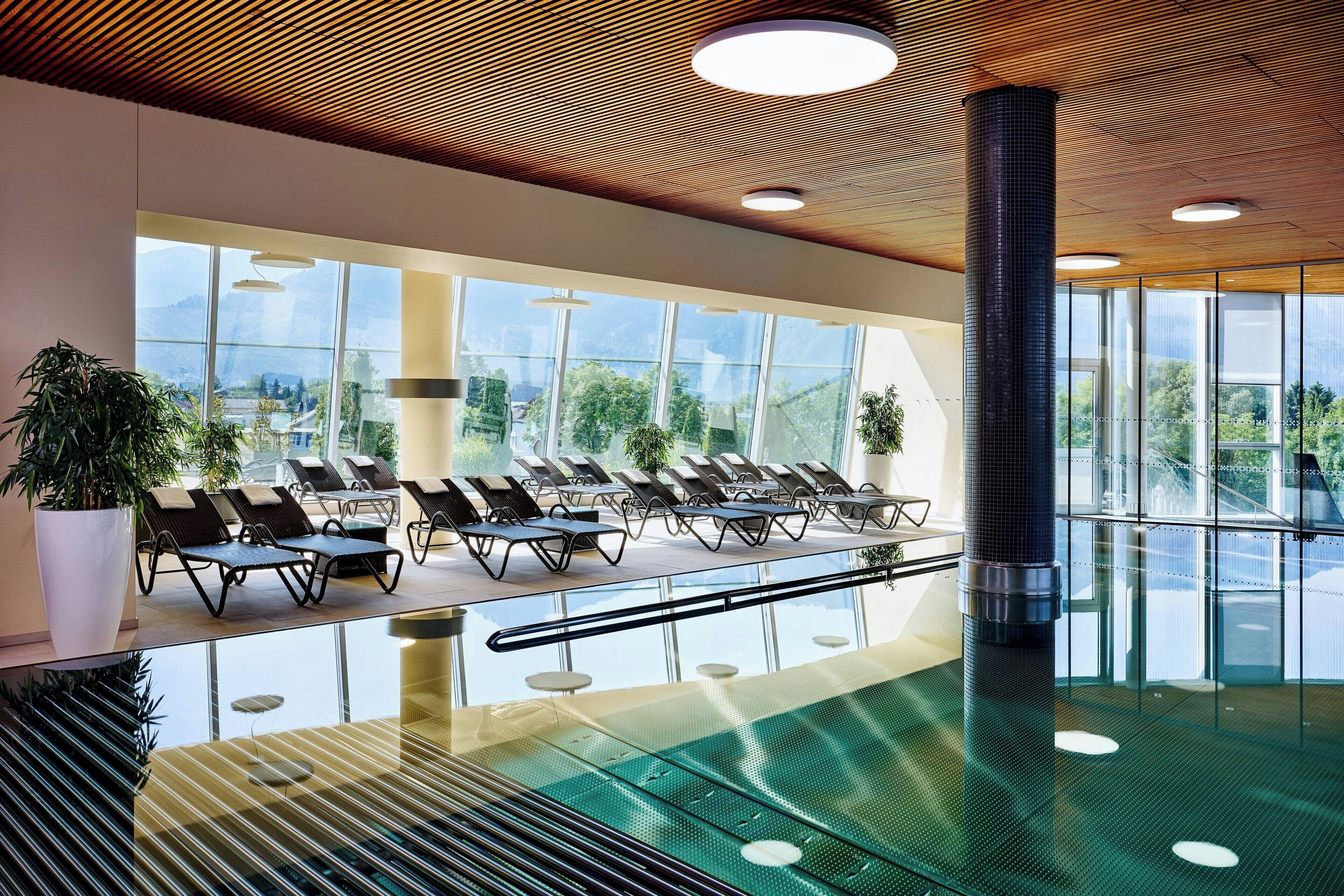 A modern indoor pool area with lounge chairs and large windows.