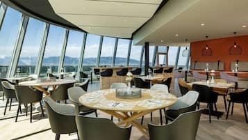 A modern dining area with round tables, chairs, and a view of mountains through large windows.