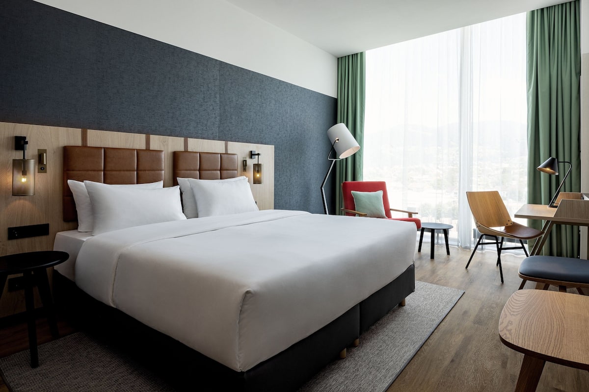 Relax in a spacious room with a large bed, wooden headboard, and a window with sheer curtains.