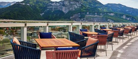 A terrace with tables and chairs, overlooking a mountainous landscape.