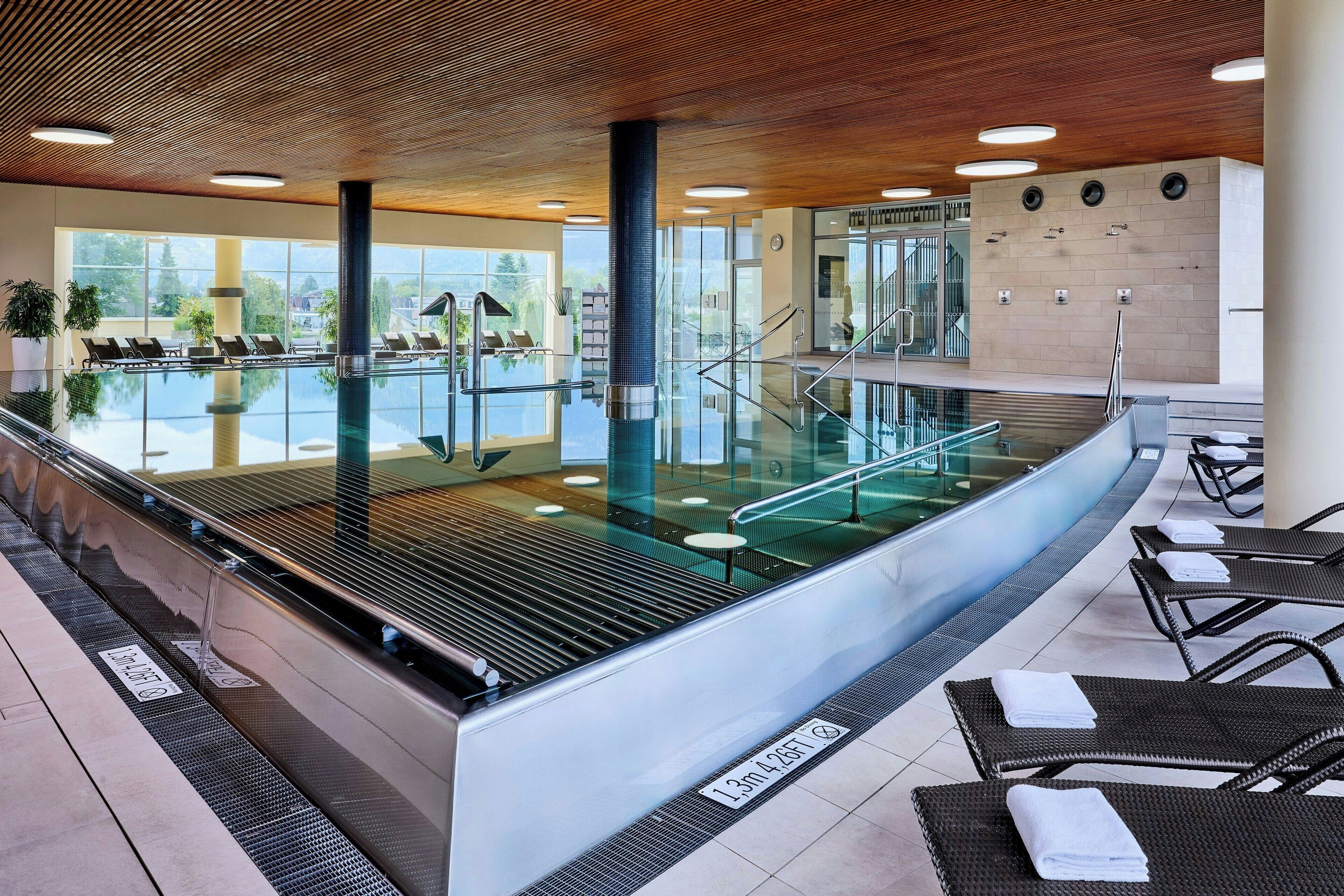 A modern indoor pool area with glass railings, lounge chairs, and a clear view of the outdoors.