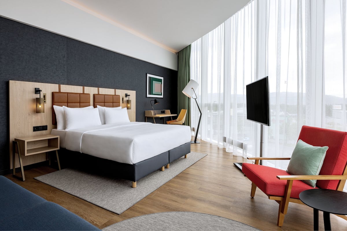 Une chambre d’hôtel moderne avec un grand lit, un bureau, une télévision et un fauteuil rouge.