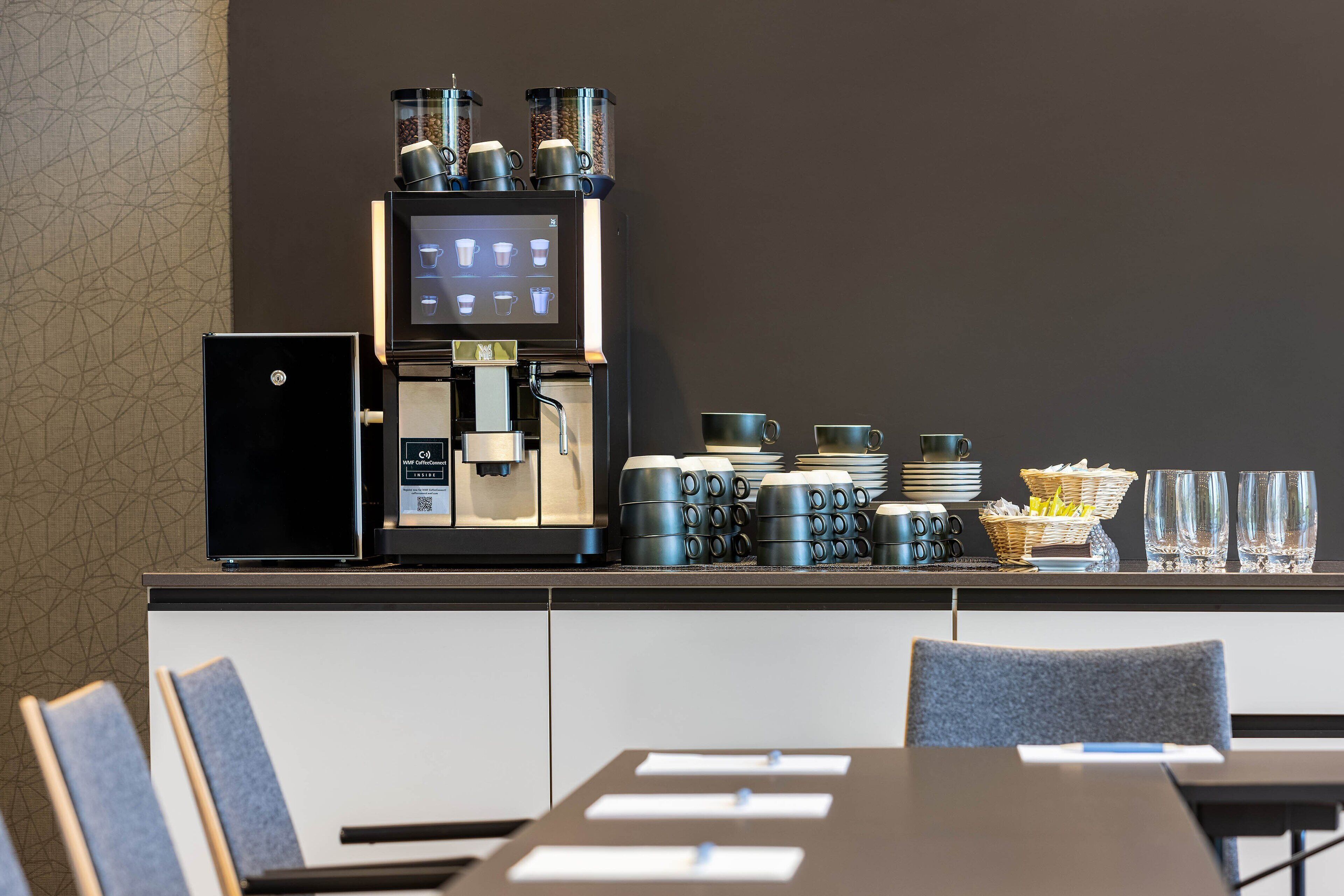 Una estación de café moderna con una máquina de café, tazas y una cesta de aperitivos.