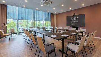A conference room with a large table, chairs, a projector screen, and large windows offering a view of the outdoors.