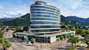 A modern hotel with a curved glass facade, located in a mountainous area with a clear sky. - Four Points By Sheraton Panoramahaus Dornbirn (Dornbirn)