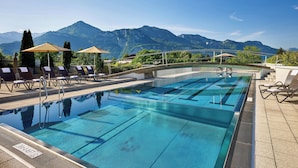 A swimming pool with lounge chairs and umbrellas, surrounded by mountains. - Four Points By Sheraton Panoramahaus Dornbirn (Dornbirn)