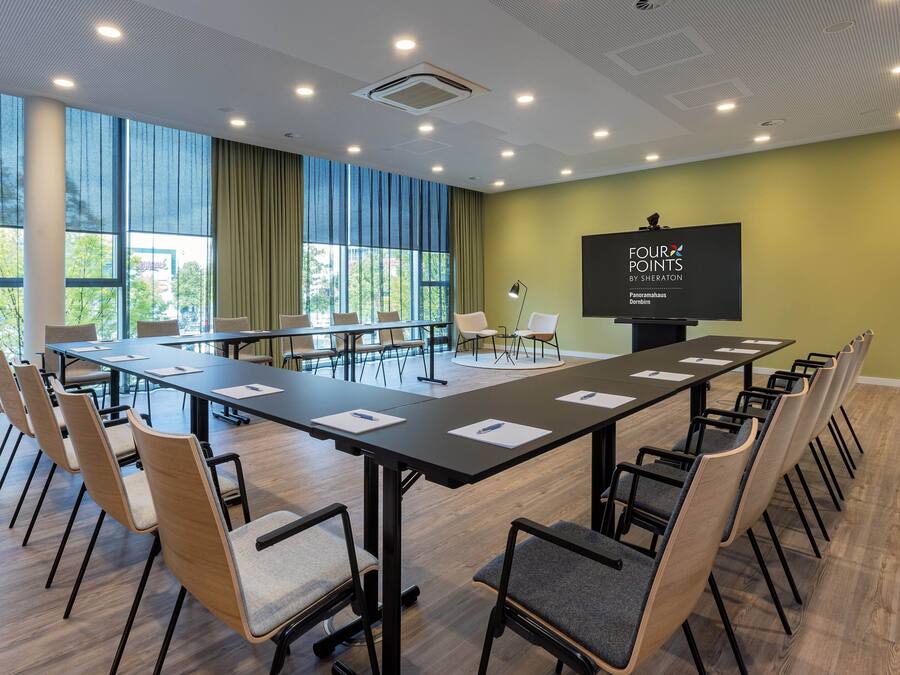 A conference room with a long table, chairs, a projector screen, and large windows.