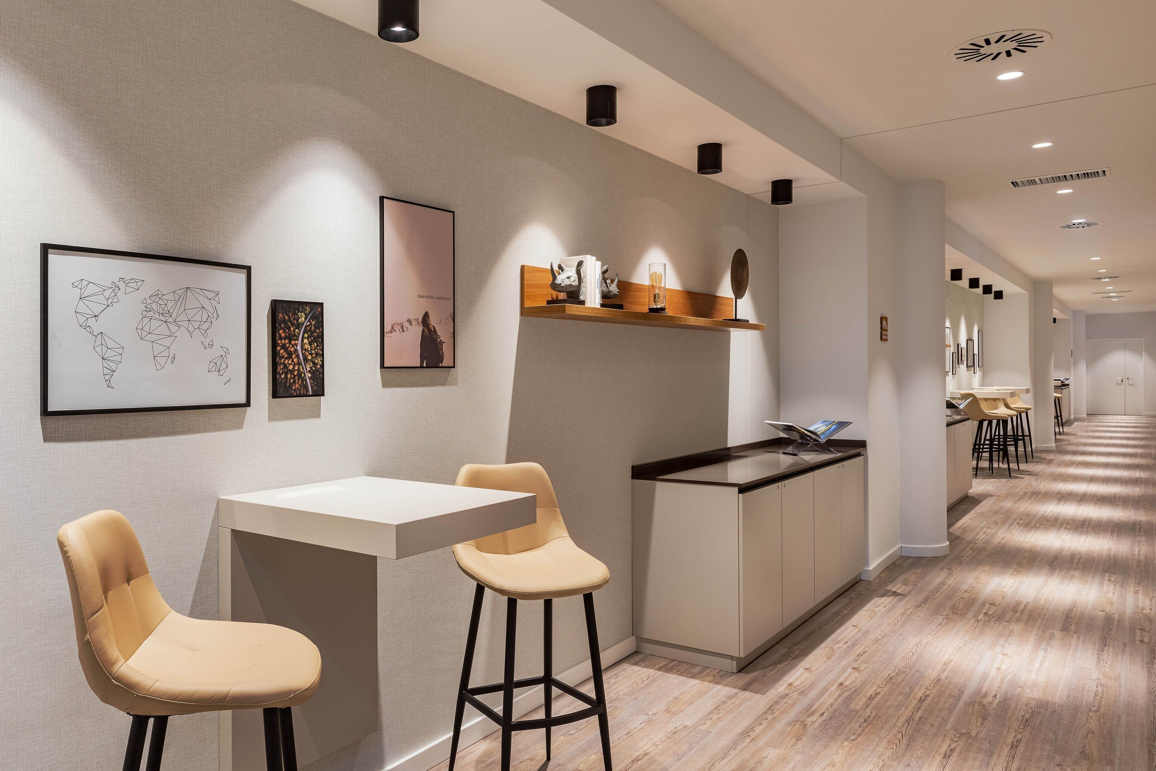 A modern kitchen with a white countertop, two beige bar stools, and a wooden shelf with kitchen items.