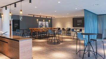 A modern bar area with a long counter, multiple seating options including bar stools and chairs, and a large screen displaying "FOUR POINTS BY SHELTON".