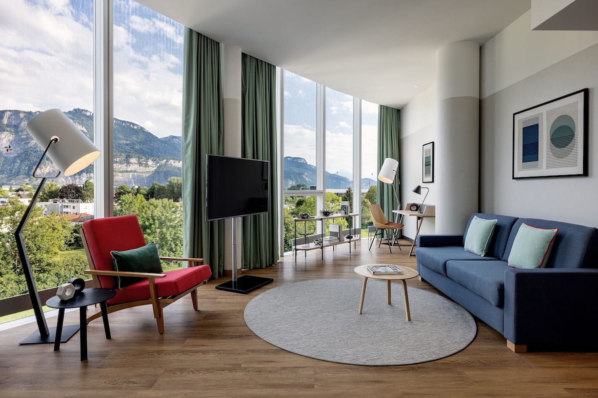Un salon moderne doté d’une grande fenêtre, d’un fauteuil rouge, d’un canapé bleu et d’un téléviseur à écran plat.
