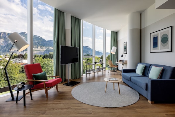 A modern living room with a large window, a red chair, a blue sofa, and a flat-screen TV.