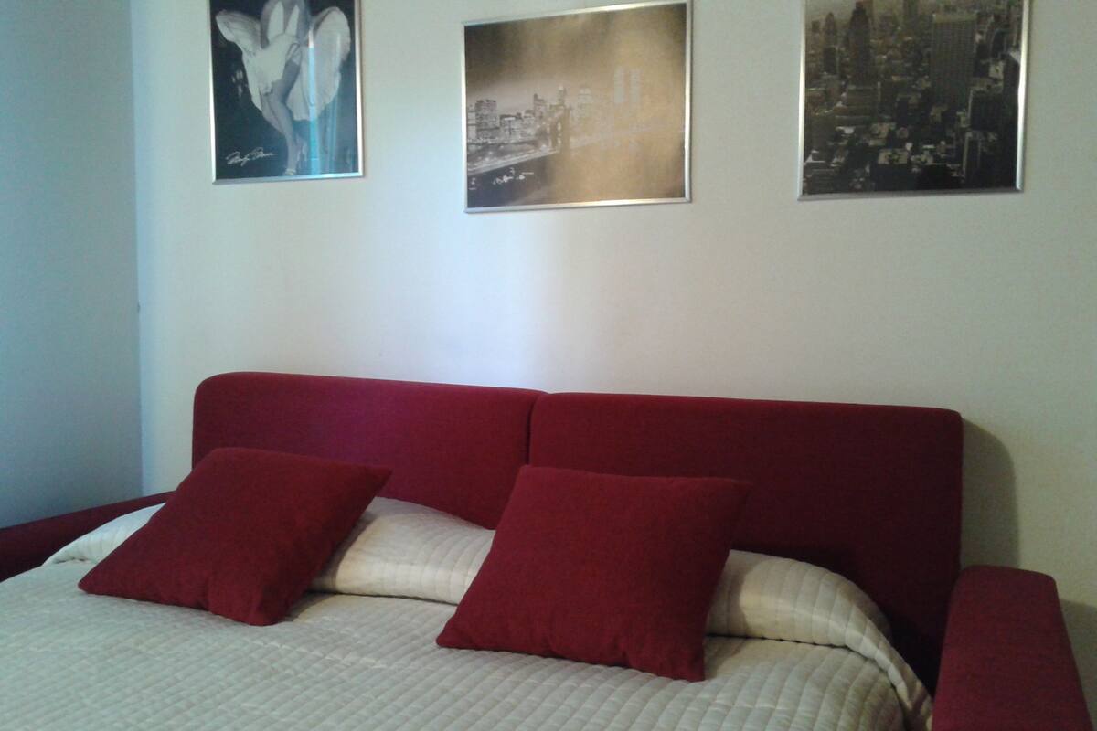 A bed with a red headboard, two red pillows, and a beige quilted bedspread.