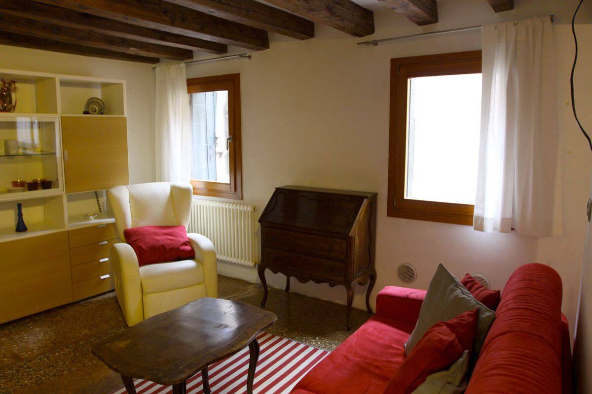 A living room with a yellow sofa, a red sofa, a wooden table, a white armchair, a wooden cabinet, and a window with curtains.