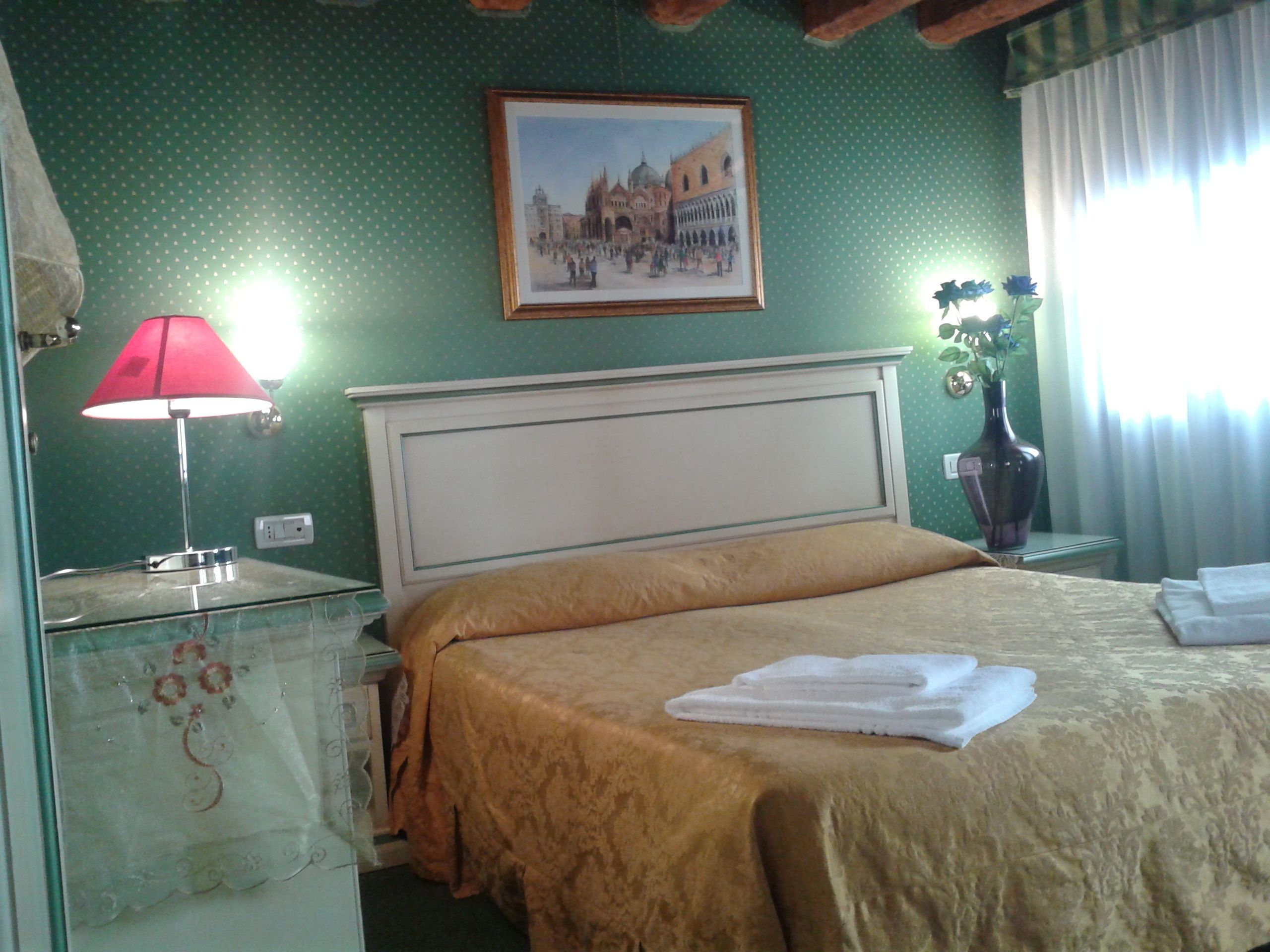A hotel room with a bed, a nightstand, a lamp, a framed picture, and a vase with flowers.