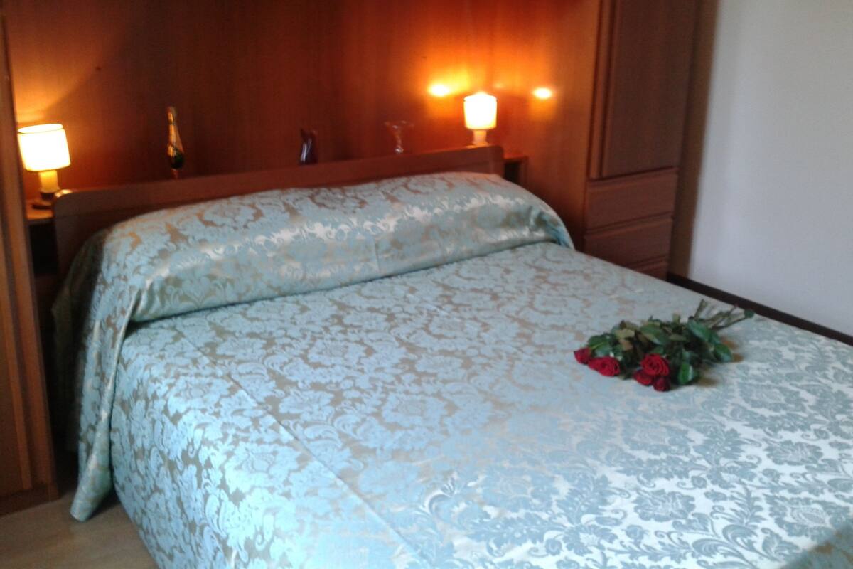 A neatly made bed with a floral bedspread, a bedside lamp, and a bouquet of flowers on the bed.