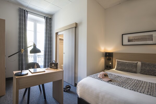 Une chambre d’hôtel avec un lit, un bureau, une chaise, une lampe et un tableau encadré au mur.