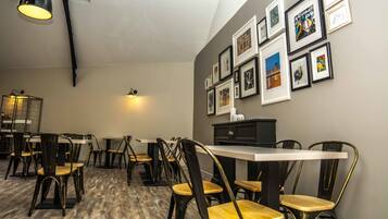 A dining area with tables and chairs, a wall with framed pictures, and a ceiling light fixture.